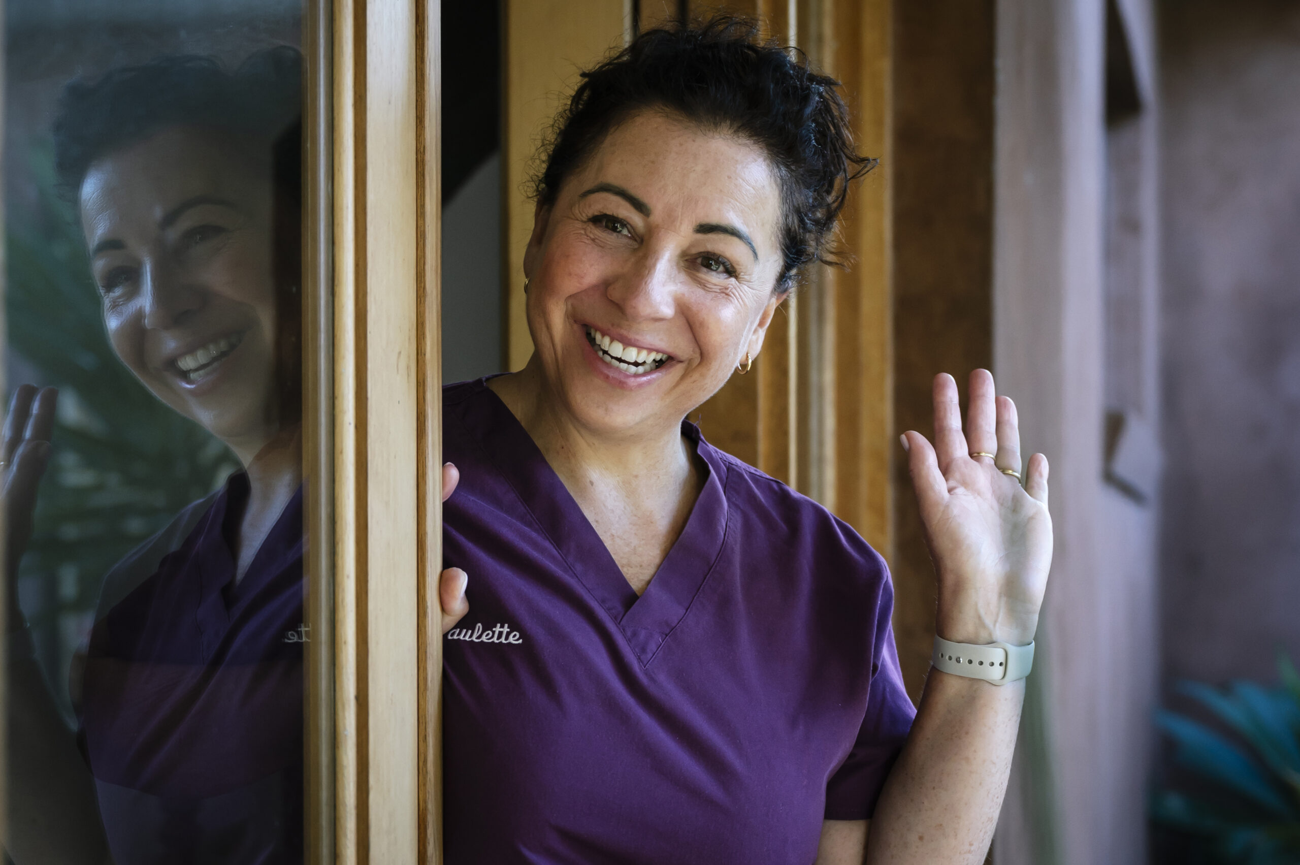 paulette smith dental hygienist is wearing a purple scrub top and standing in the doorway waving to welcome new clients